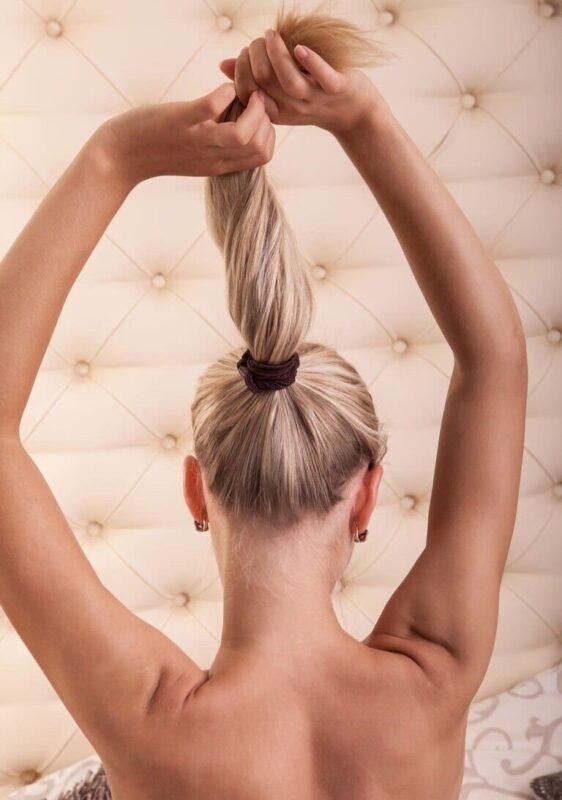 yankee doodle dandy - a woman with blonde hair tied in a long ponytail twisting and pulling her ponytail straight up - viewed from behind